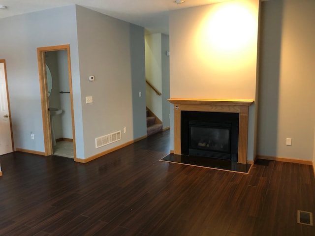 unfurnished living room featuring visible vents, a fireplace with flush hearth, wood finished floors, and stairway