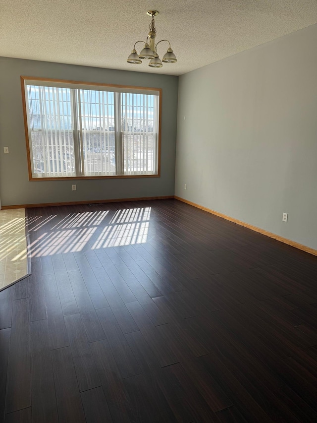 empty room with an inviting chandelier, dark wood-style floors, baseboards, and a textured ceiling