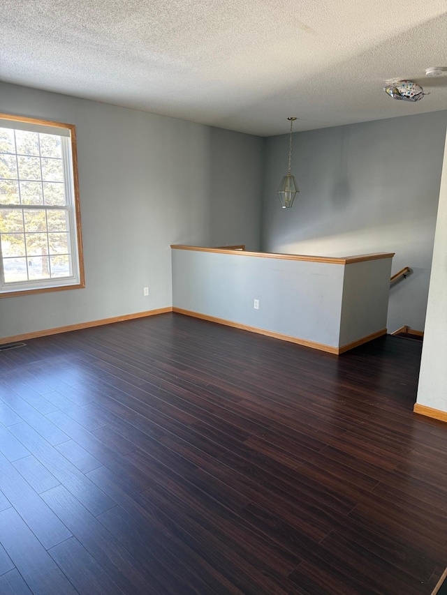 empty room featuring baseboards, a textured ceiling, and dark wood finished floors