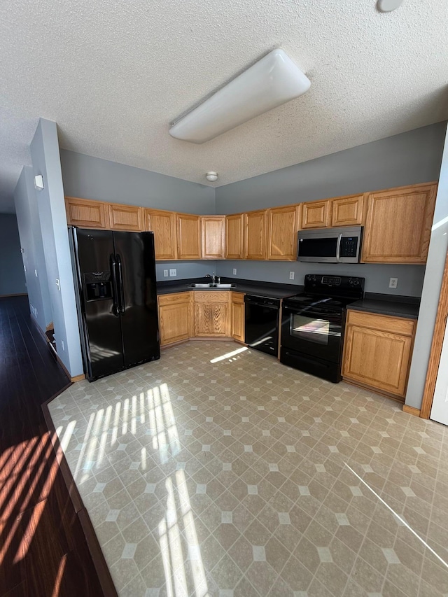 kitchen with baseboards, a sink, black appliances, a textured ceiling, and dark countertops