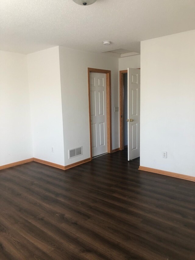 spare room featuring baseboards, visible vents, dark wood-style flooring, and a textured ceiling