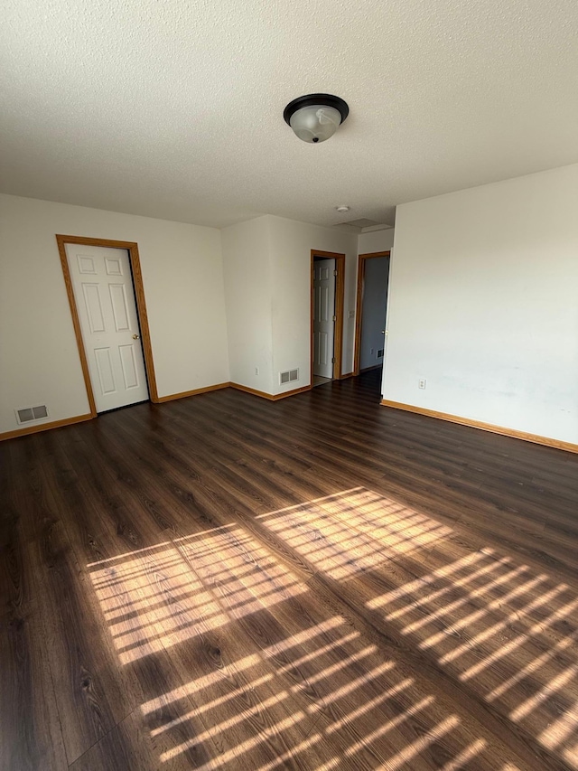 empty room featuring baseboards, visible vents, dark wood-style flooring, and a textured ceiling