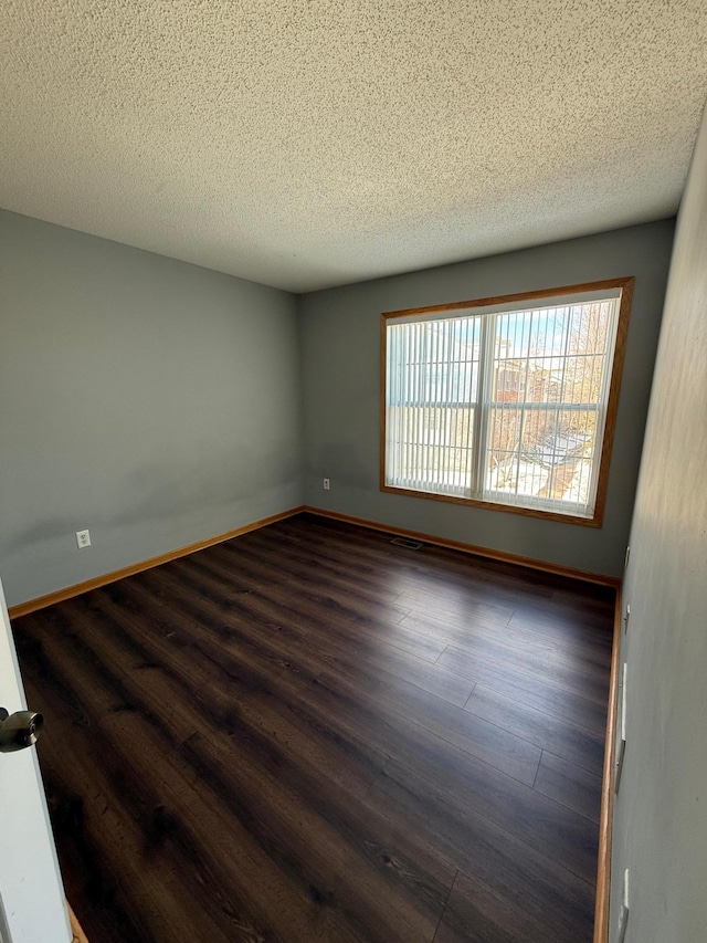 spare room with dark wood-style floors, a textured ceiling, and baseboards