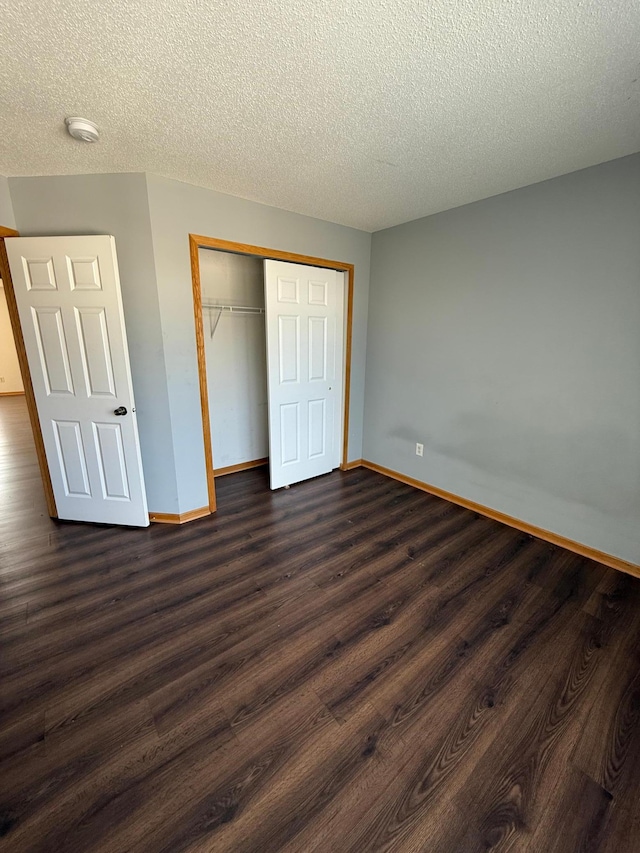 unfurnished bedroom with dark wood-style floors, a textured ceiling, a closet, and baseboards