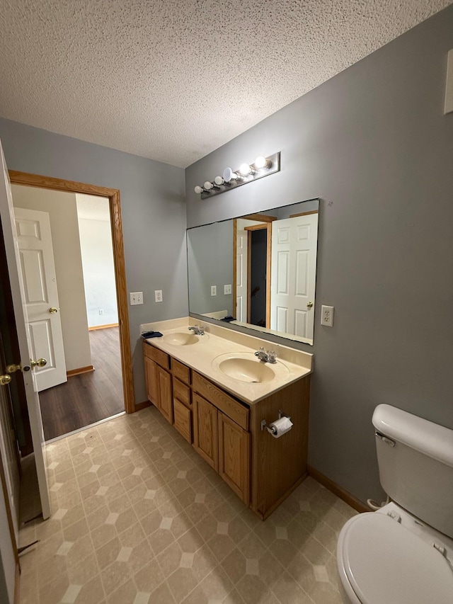 bathroom featuring double vanity, a textured ceiling, toilet, and a sink