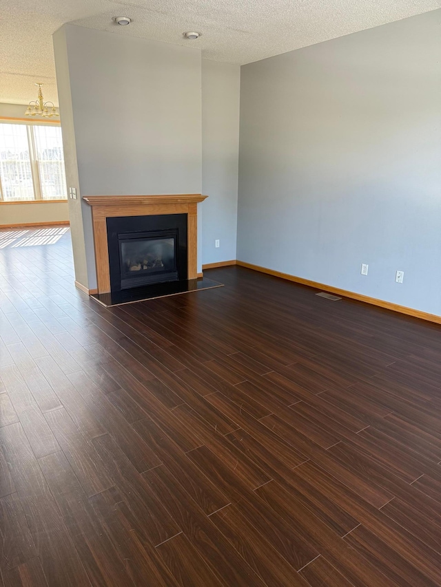 unfurnished living room with a textured ceiling, a glass covered fireplace, dark wood-style floors, baseboards, and a chandelier