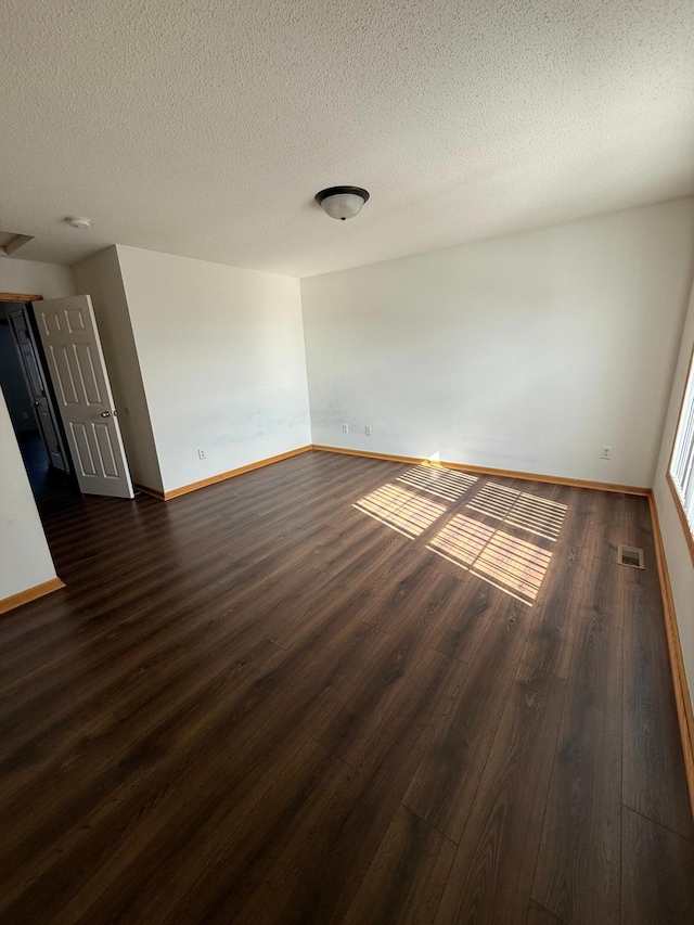 spare room featuring dark wood-type flooring, baseboards, visible vents, and a textured ceiling