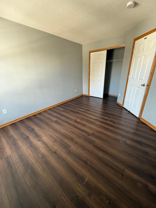unfurnished bedroom featuring dark wood finished floors, baseboards, a closet, and a textured ceiling
