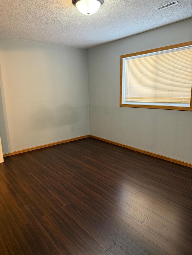 empty room featuring dark wood-style floors, visible vents, a textured ceiling, and baseboards