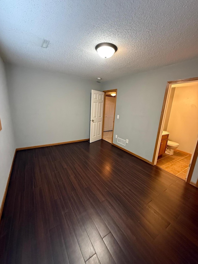 empty room with dark wood-style floors, visible vents, a textured ceiling, and baseboards