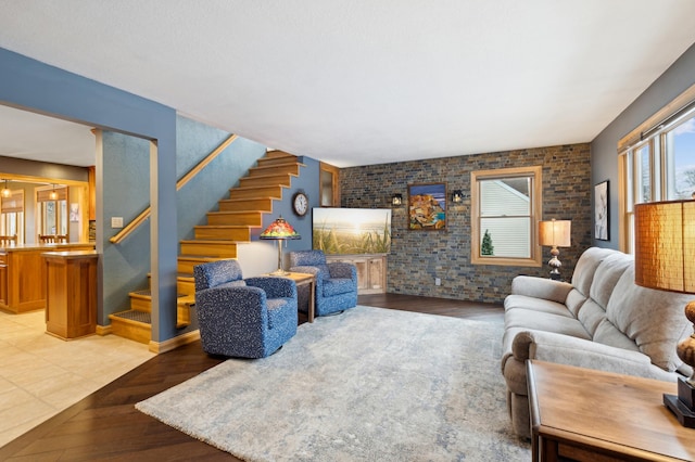 living area featuring light wood-style floors, brick wall, and stairs