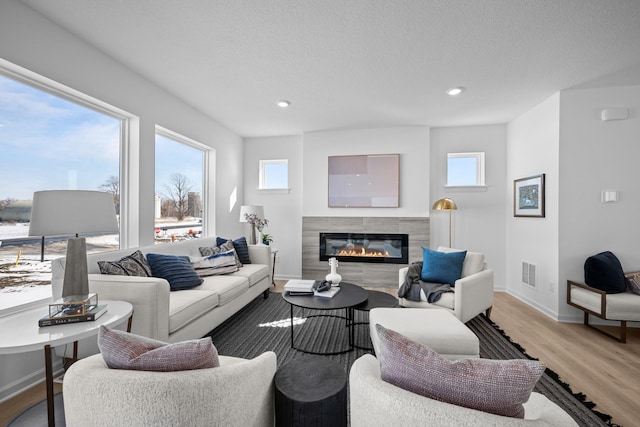 living area with visible vents, light wood-style flooring, plenty of natural light, and a glass covered fireplace