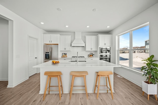 kitchen with stainless steel appliances, a kitchen island with sink, custom range hood, and a kitchen breakfast bar