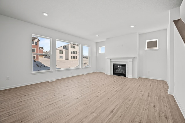 unfurnished living room featuring light wood finished floors, recessed lighting, a wealth of natural light, and a glass covered fireplace