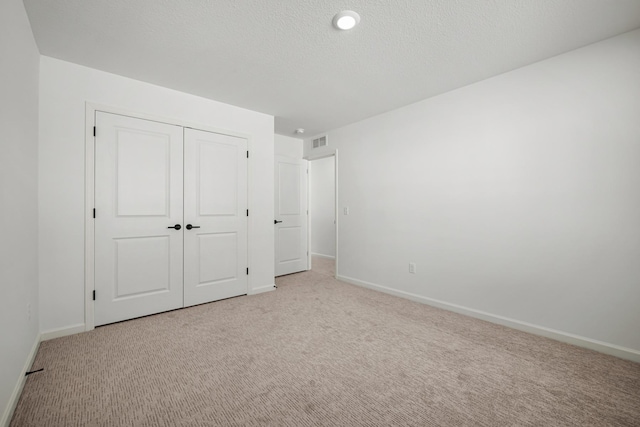 unfurnished bedroom with a textured ceiling, a closet, baseboards, and light colored carpet