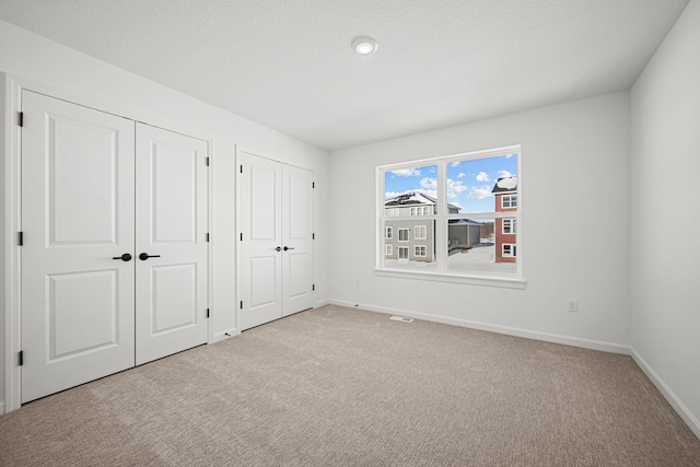 unfurnished bedroom with carpet flooring, visible vents, baseboards, and two closets