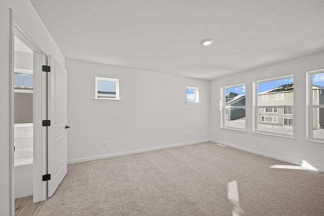 unfurnished room featuring light carpet, a textured ceiling, and baseboards