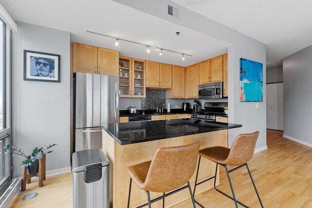 kitchen featuring visible vents, light wood-style floors, appliances with stainless steel finishes, a kitchen bar, and glass insert cabinets