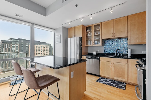 kitchen with a kitchen breakfast bar, stainless steel appliances, light wood-style floors, light brown cabinets, and a sink