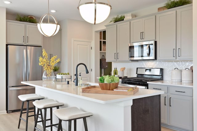 kitchen with tasteful backsplash, appliances with stainless steel finishes, light countertops, and an island with sink