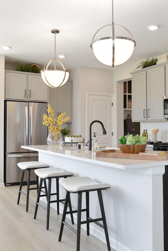 kitchen featuring a kitchen bar, light wood-style flooring, decorative light fixtures, appliances with stainless steel finishes, and light countertops