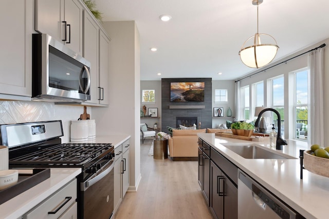 kitchen with a sink, stainless steel appliances, a large fireplace, light wood finished floors, and light countertops