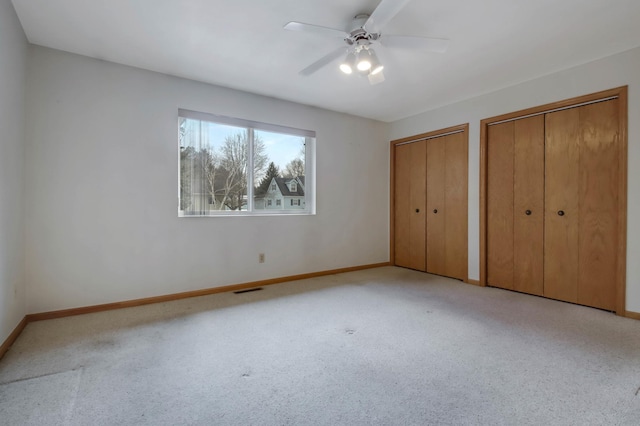 unfurnished bedroom with carpet flooring, a ceiling fan, visible vents, baseboards, and two closets