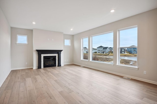 unfurnished living room featuring recessed lighting, visible vents, baseboards, light wood finished floors, and a glass covered fireplace