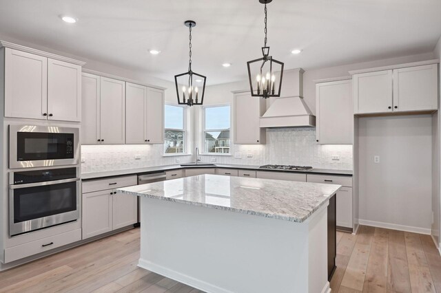 kitchen with stainless steel appliances, light wood-style floors, premium range hood, and a kitchen island