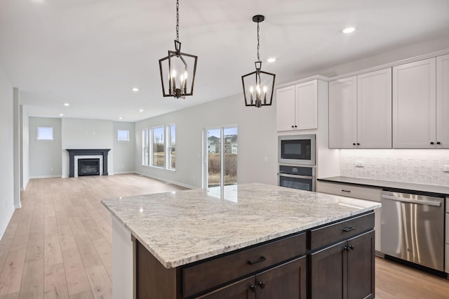 kitchen with a fireplace, stainless steel appliances, tasteful backsplash, light wood-style floors, and white cabinetry