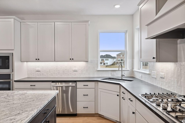 kitchen featuring decorative backsplash, light wood-style floors, appliances with stainless steel finishes, wall chimney range hood, and a sink