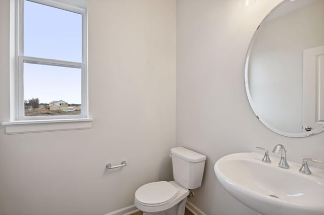 half bath with baseboards, a sink, and toilet