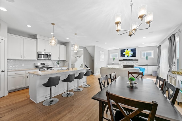 dining area with a stone fireplace, stairway, recessed lighting, and light wood-style floors