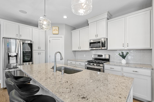 kitchen with a kitchen island with sink, stainless steel appliances, a sink, white cabinetry, and backsplash