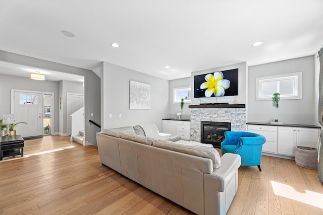 living area with a stone fireplace, recessed lighting, baseboards, light wood-style floors, and stairway