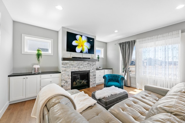 living area with light wood-style flooring, recessed lighting, a stone fireplace, and baseboards