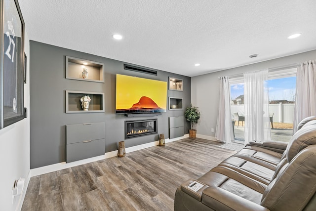 living room with recessed lighting, a glass covered fireplace, a textured ceiling, wood finished floors, and baseboards