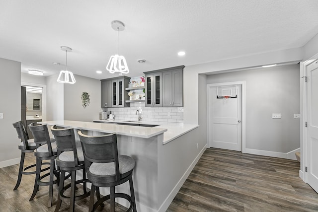 kitchen featuring dark wood-style floors, a breakfast bar, gray cabinets, light countertops, and a peninsula