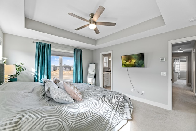 bedroom with a tray ceiling, carpet flooring, ceiling fan, ensuite bath, and baseboards