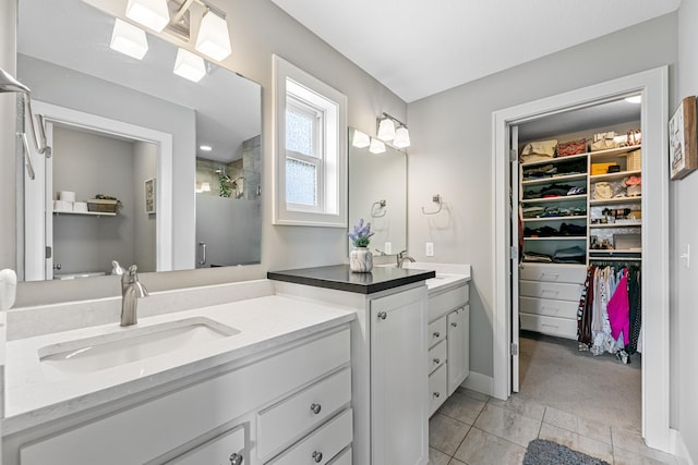 bathroom with tile patterned floors, a sink, a walk in closet, walk in shower, and two vanities