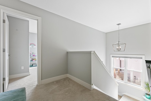 hall featuring carpet floors, baseboards, a chandelier, and an upstairs landing