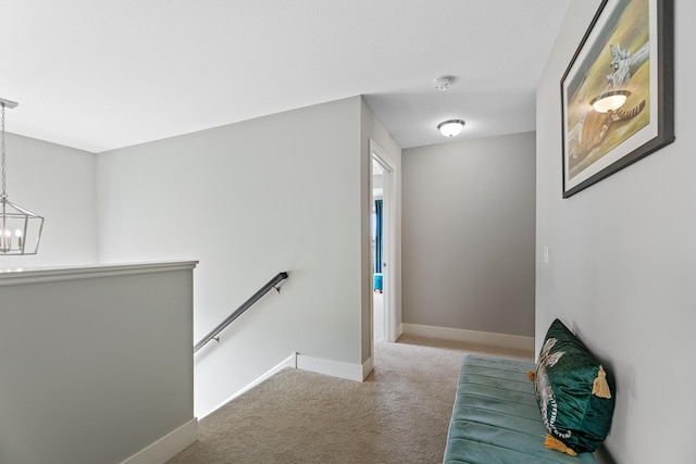 corridor with baseboards, carpet flooring, a notable chandelier, and an upstairs landing