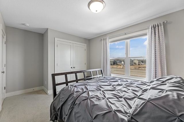 bedroom featuring a closet, light carpet, a textured ceiling, and baseboards