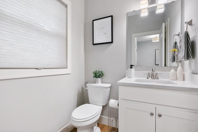 half bath with toilet, wood finished floors, vanity, and baseboards