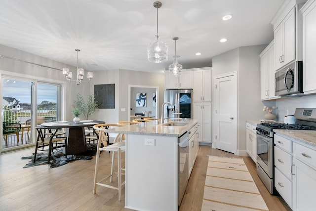 kitchen with a sink, appliances with stainless steel finishes, recessed lighting, light wood finished floors, and a center island with sink