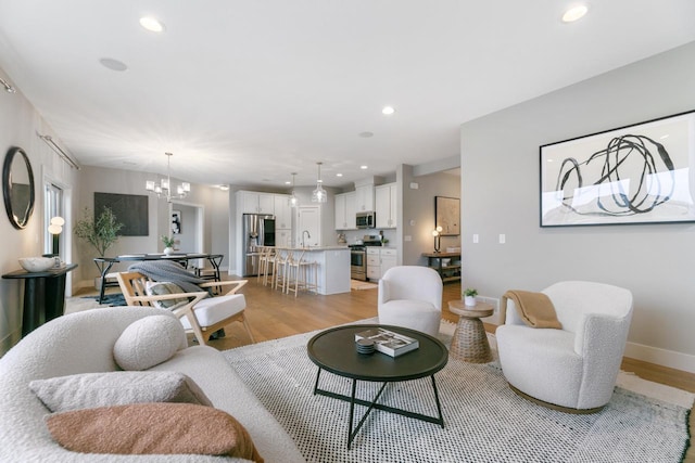 living area featuring baseboards, recessed lighting, a notable chandelier, and light wood-style floors