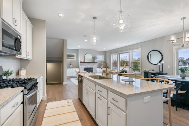 kitchen with a kitchen island with sink, light wood-style floors, appliances with stainless steel finishes, backsplash, and a sink