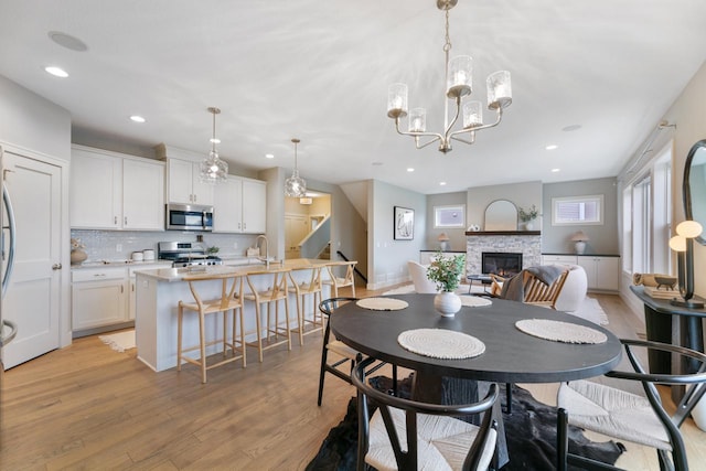 dining room featuring recessed lighting, stairs, light wood-style flooring, a fireplace, and a notable chandelier