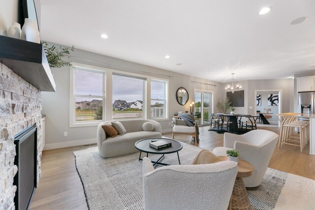 living area with light wood-type flooring, baseboards, a chandelier, and a fireplace
