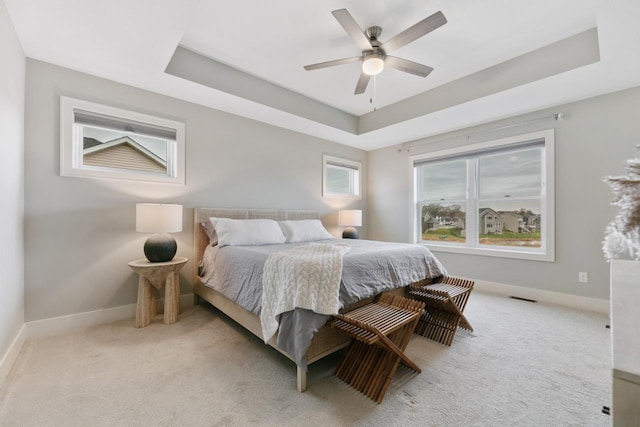 bedroom with a raised ceiling, baseboards, a ceiling fan, and light carpet